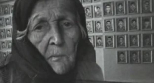 An elderly woman near the photos of the victims of war and deportation. Photo: screenshot of the video on the YouTube channel vainakh38